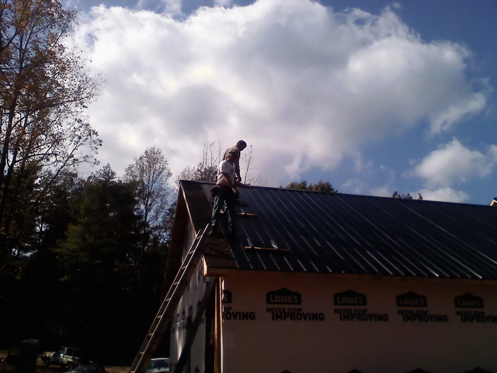 Roofer fastening dark metal panels high against a cloudy sky, from a Roof Inspection job in Avon