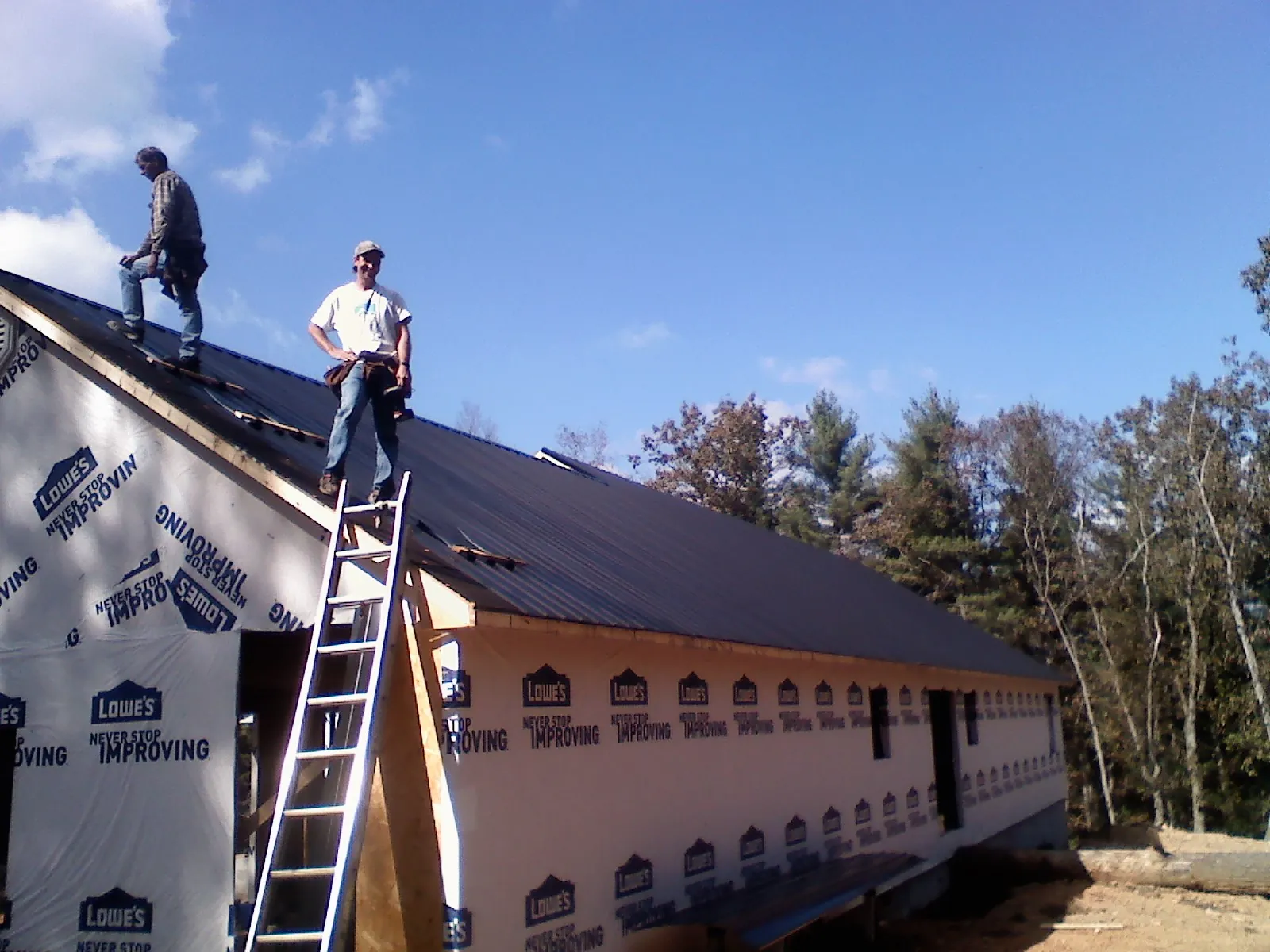 Two roofers standing on a long dark metal roof over a wrapped building in Avon